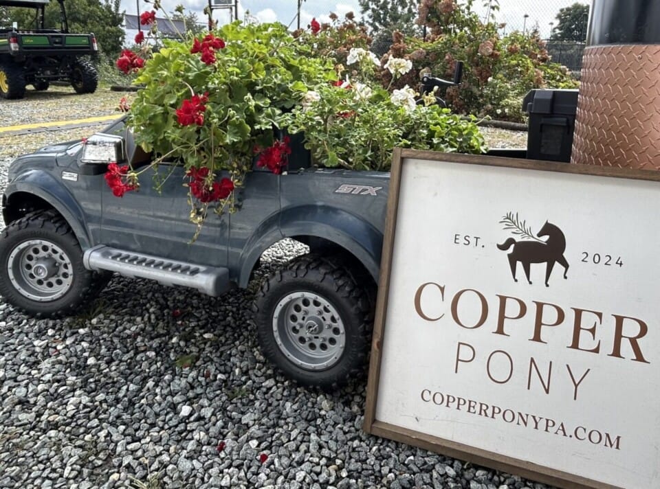 Copper Pony - A gray toy truck filled with red and white flowers is parked on gravel next to a Copper Pony sign displaying a horse logo and the website copperponypa.com.