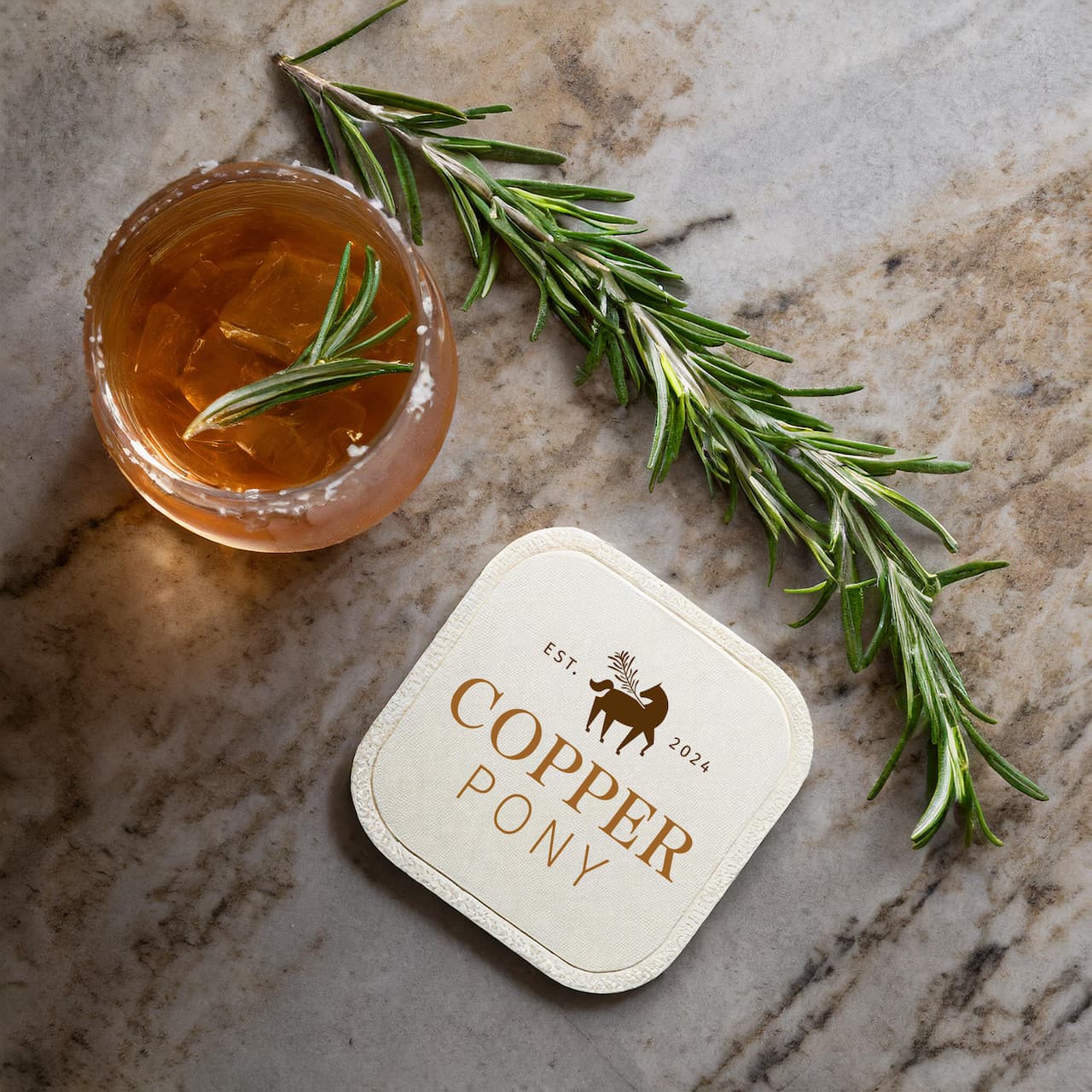 image of a Copper Pony drink coaster on granite surface with a fresh cocktail and sprig of rosemary